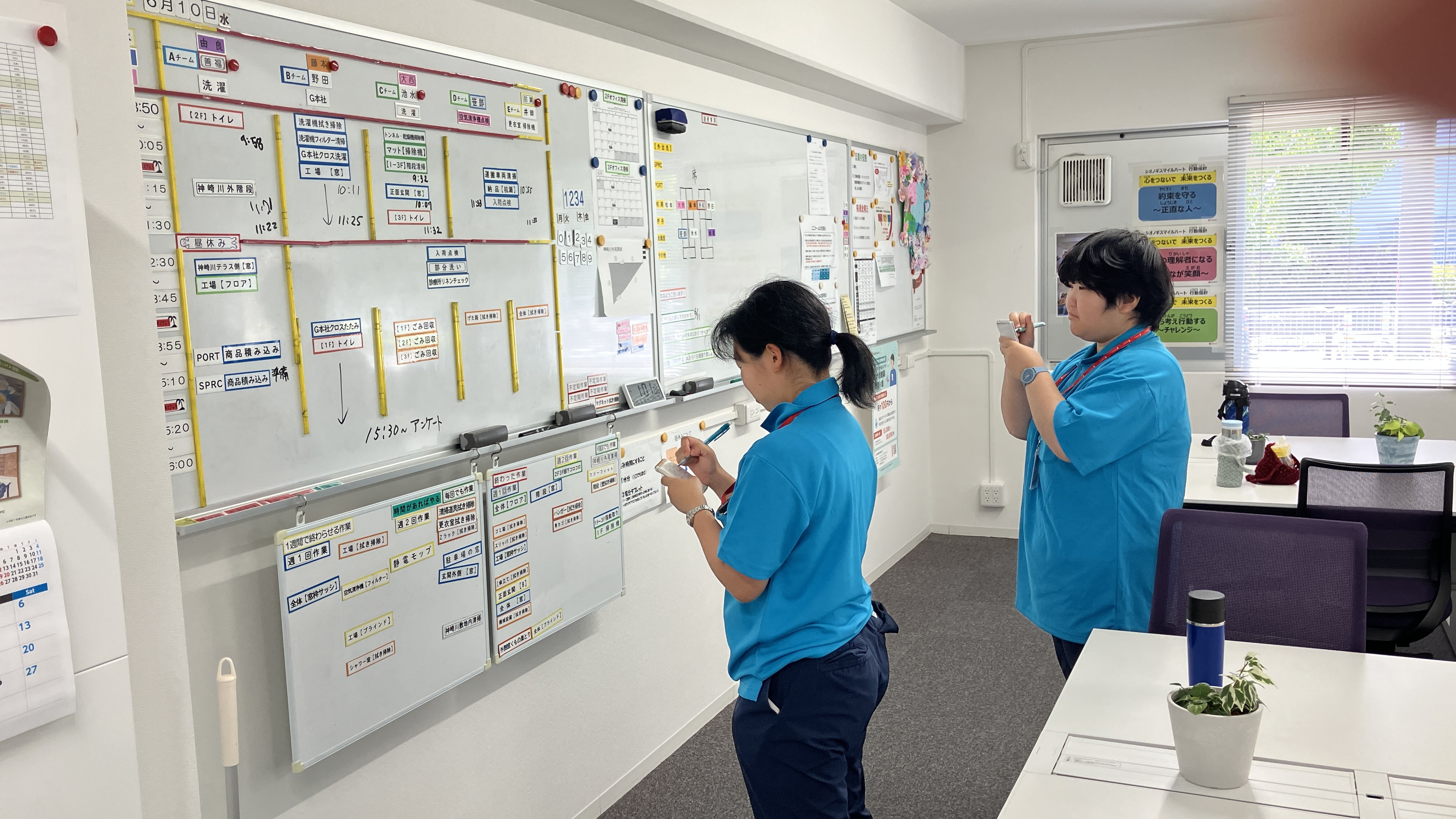 障がいのある方２名が、ホワイトボードの前で今日一日の作業スケジュールをメモしている写真です。