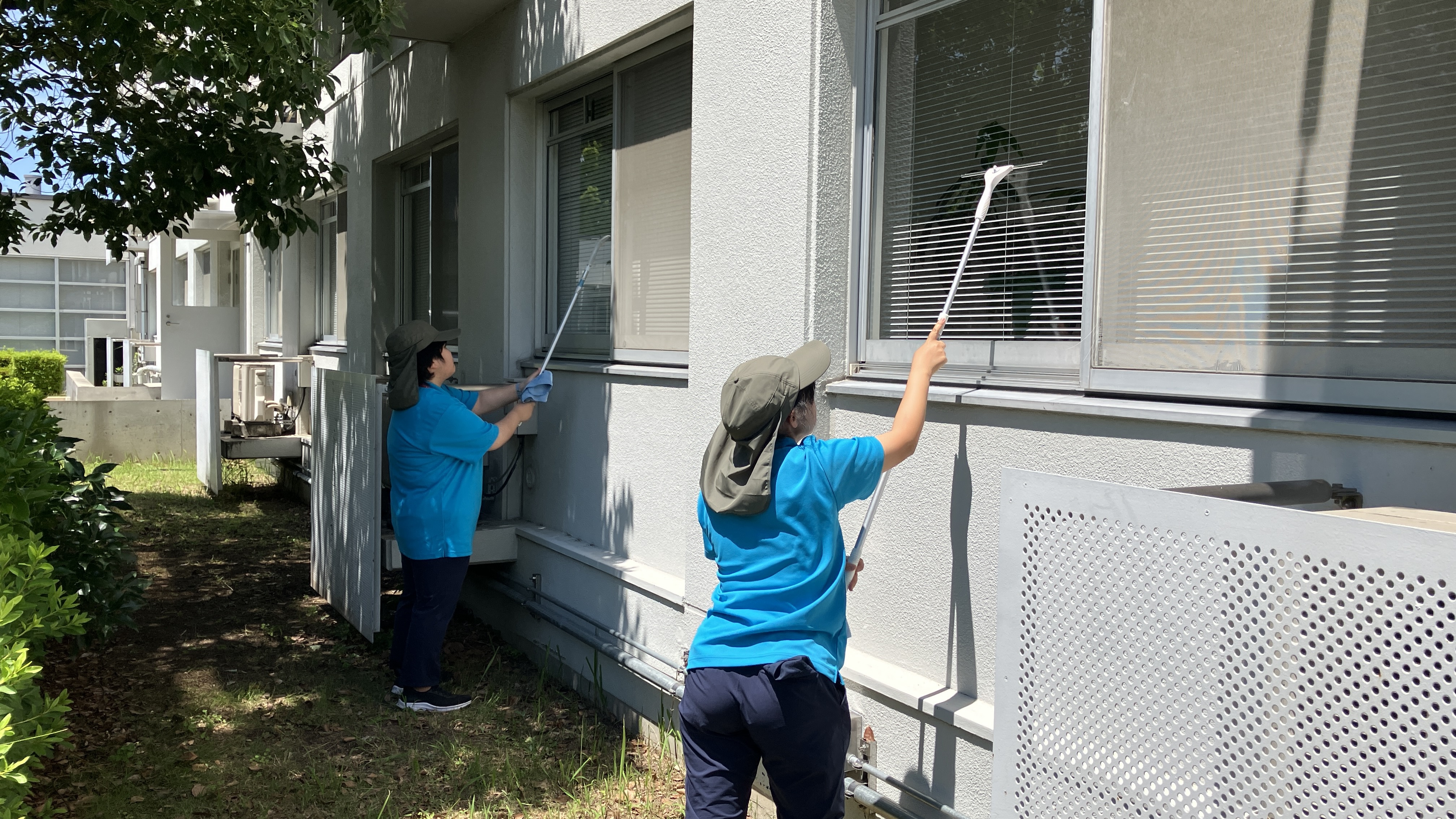 障がいのある方２名が、建物の屋外の窓清掃を水切りワイパーを使用してしている写真です。